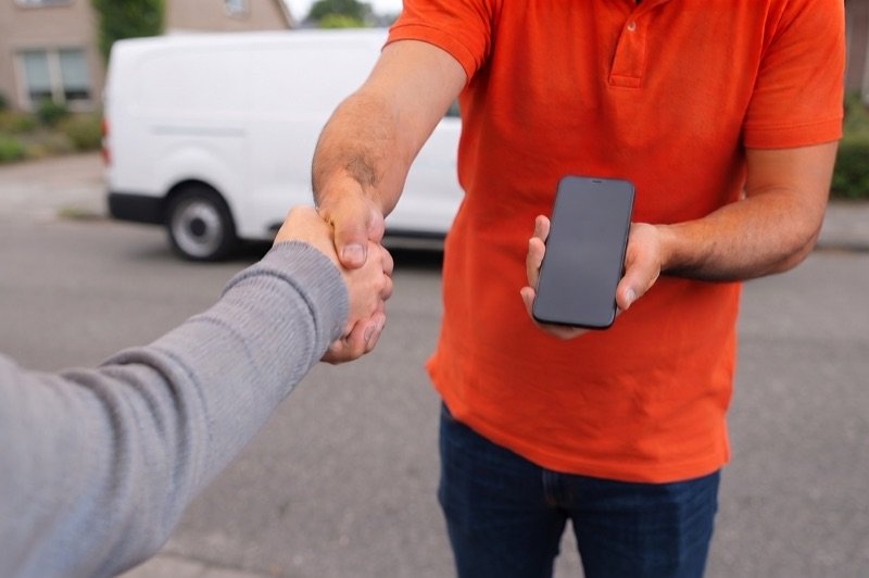 A technician shaking the customer's hand across the repair mat while handing back the finished phone.